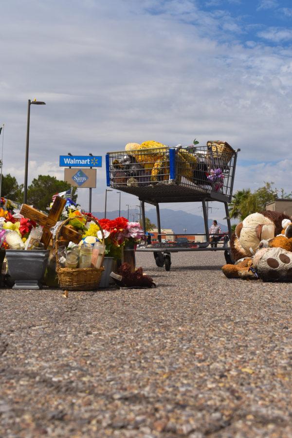 A shopping cart stands alone in the street of the original site, before the opening of the walmart filled with teddy bears and flowers after being moved away from puddles created by rainfall.